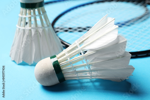 Feather badminton shuttlecocks and rackets on light blue background, closeup