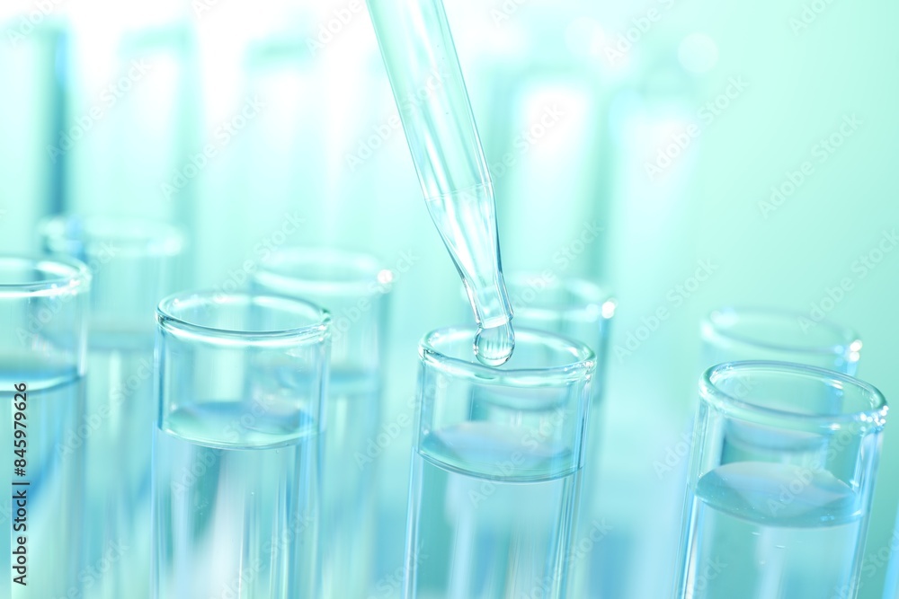 Dripping liquid from pipette into test tube on turquoise background, closeup Dripping liquid from pipette into test tube on turquoise background, closeup