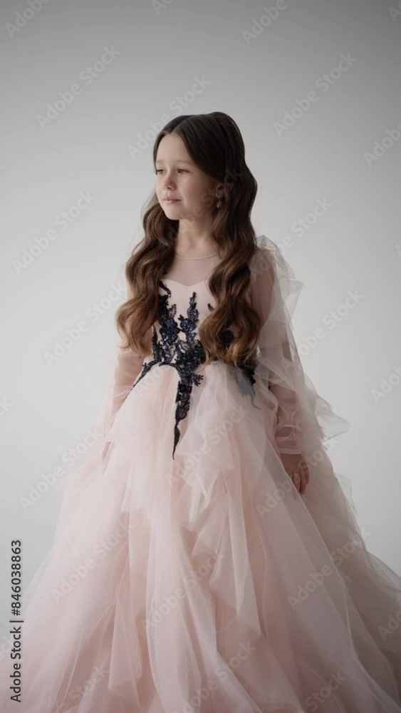 Little princess in elegant festive outfit. Girl in long pink dress poses on white background. Concept of holiday, beauty, innocence Little princess in elegant festive outfit. Girl in long pink dress poses on white background. Concept of holiday, beauty, innocence