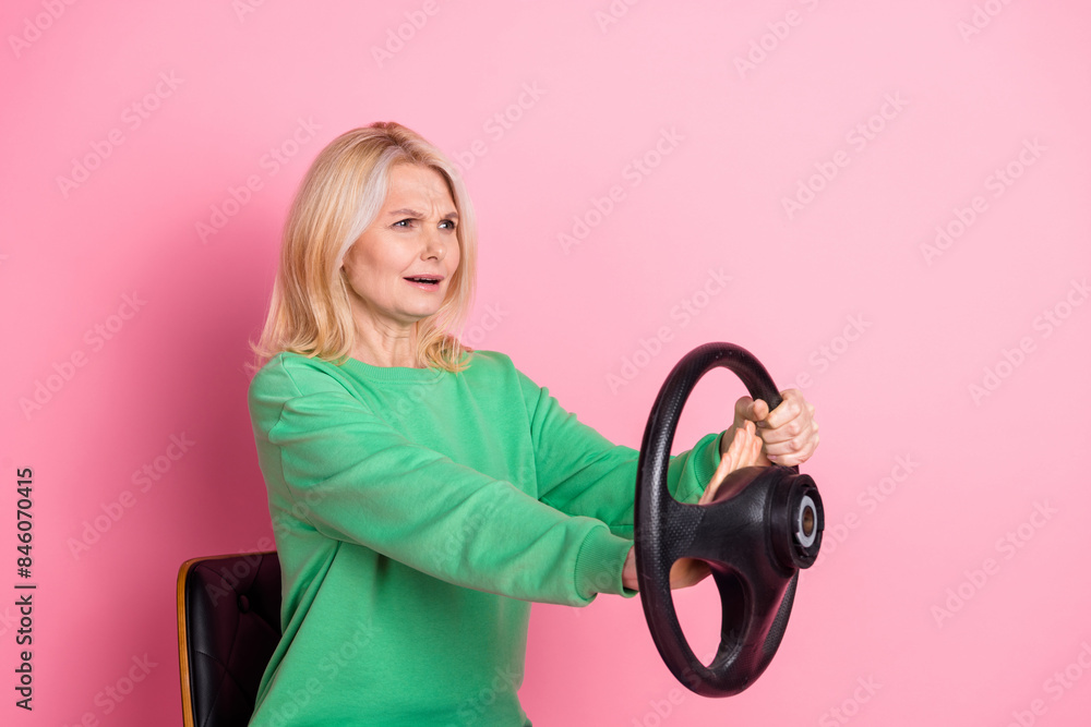 Photo portrait of lovely senior lady hold steering wheel honk nervous dressed stylish green garment isolated on pink color background Photo portrait of lovely senior lady hold steering wheel honk nervous dressed stylish green garment isolated on pink color background