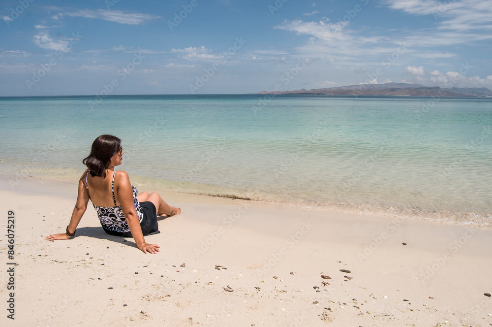 Mexican Latin woman, sitting in the sand of a beautiful beach in La Paz Baja California Sur, enjoying a summer vacation, in the background, Espiritu Santo Island. Baja style suntan. MEXICO. Mexican Latin woman, sitting in the sand of a beautiful beach in La Paz Baja California Sur, enjoying a summer vacation, in the background, Espiritu Santo Island. Baja style suntan. MEXICO.