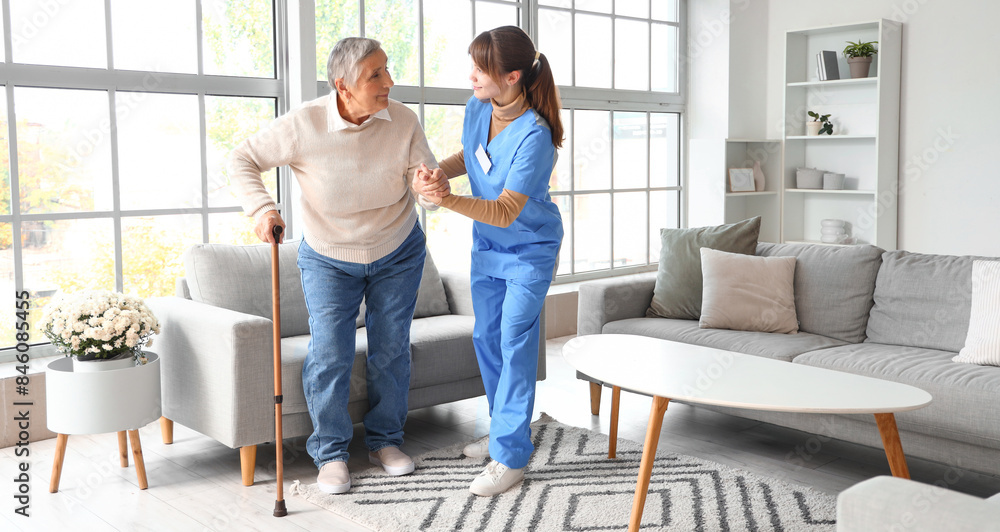 Obraz premium Young caregiver helping senior woman to walk at home