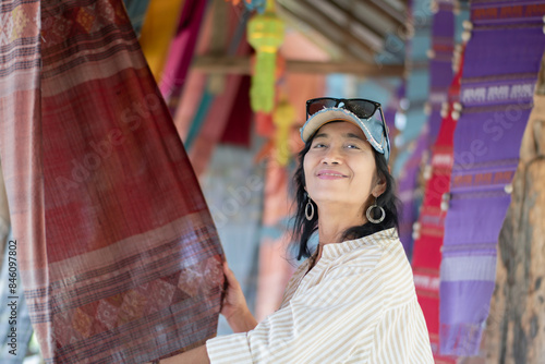 Asian mid adult woman holding woven fabric which was decorated on ceiling of local cafe for tourist watching and taking photos, soft focus, happiness of humans concept.