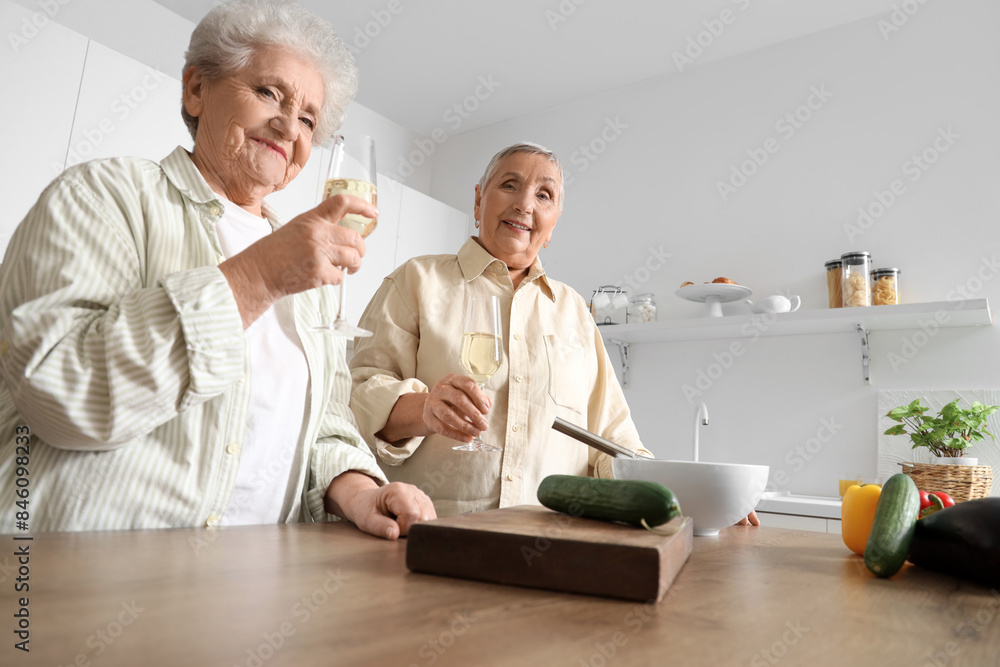 Senior female friends drinking champagne while cooking in kitchen Senior female friends drinking champagne while cooking in kitchen