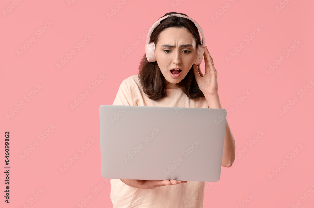Confused young woman with laptop and headphones on pink background Confused young woman with laptop and headphones on pink background