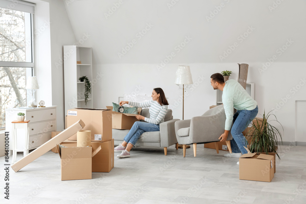 Happy young couple carrying armchair in room on moving day Happy young couple carrying armchair in room on moving day