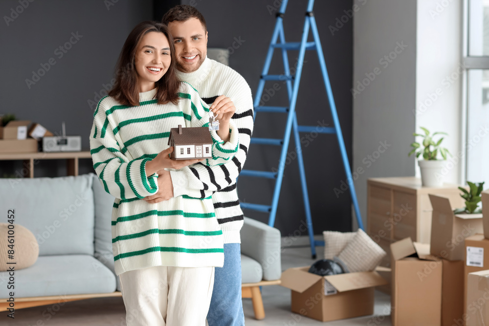 Happy young couple with keys and house model in room on moving day Happy young couple with keys and house model in room on moving day