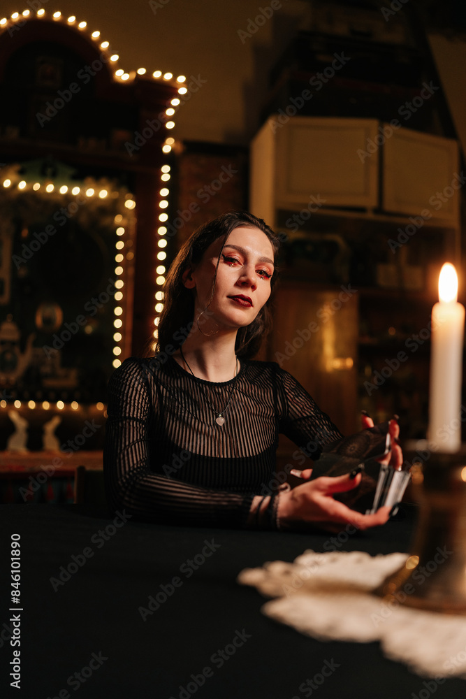 Vertical portrait of mysterious fortuneteller shuffling deck of tarot cards by light of burning candles, looking at camera with serious expression. Warlock performing esoteric rite, forecasting fate. Vertical portrait of mysterious fortuneteller shuffling deck of tarot cards by light of burning candles, looking at camera with serious expression. Warlock performing esoteric rite, forecasting fate.