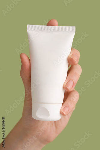 Female hand with tube of cream on green background, closeup