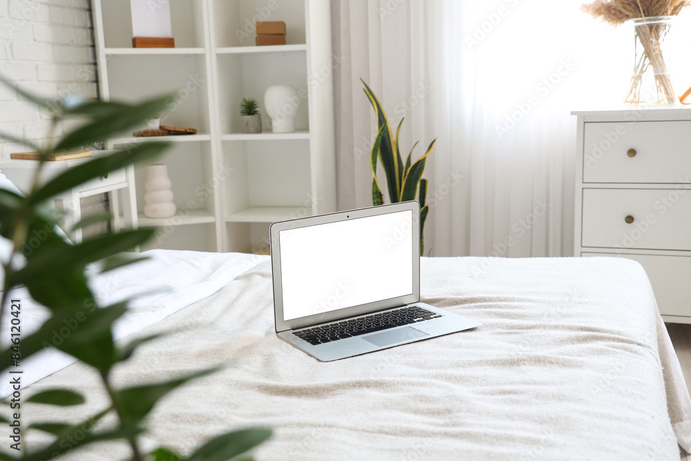 Fototapeta premium Interior of light bedroom with houseplant and laptop on white bed