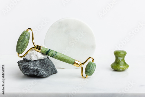 Green jade roller massager for face on white marble.