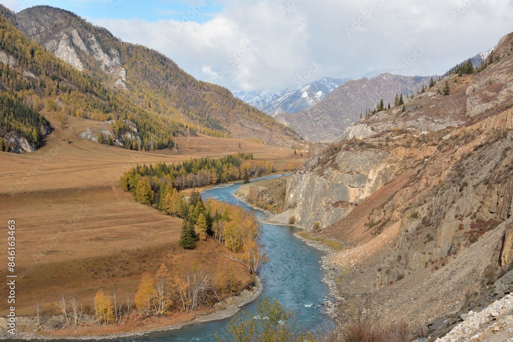 Fototapeta premium A beautiful turbulent river flowing through a mountain valley on a cloudy day in early autumn.
