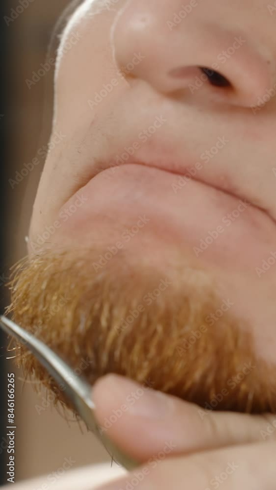 Vertical video. Young Man Trimming Red Beard with Scissors in Front of Mirror, Hair Falling Down, Slow Motion. Vertical video. Young Man Trimming Red Beard with Scissors in Front of Mirror, Hair Falling Down, Slow Motion.