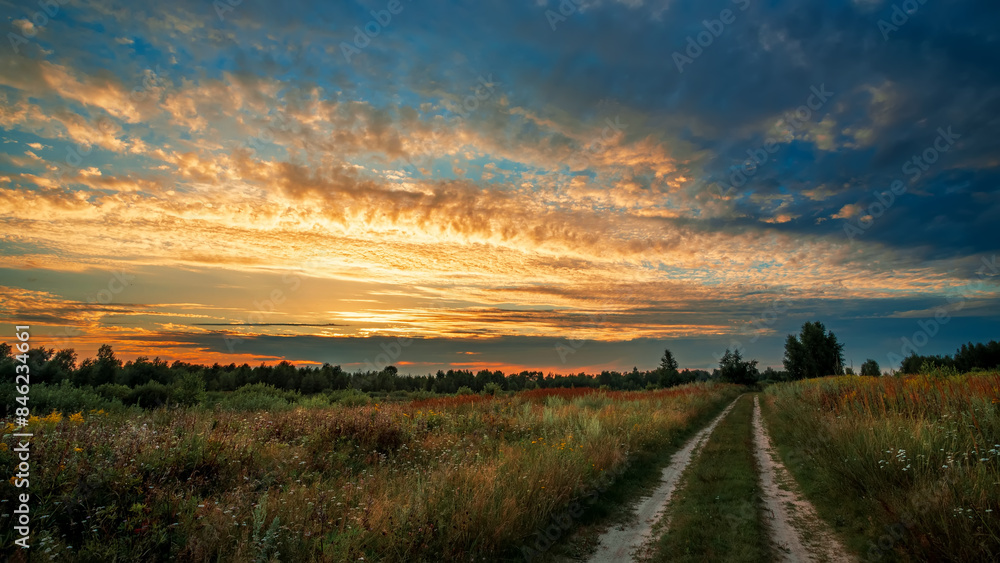 Rural road in a field against the backdrop of a summer sunset. Rural road in a field against the backdrop of a summer sunset.