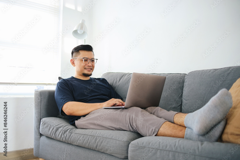 Asian Man Working On Laptop Sitting On Sofa At Home. Remote Job. Asian Man Working On Laptop Sitting On Sofa At Home. Remote Job.