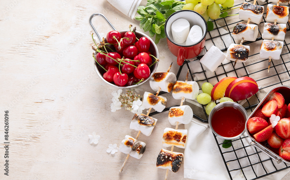Marshmallow skewers and and strawberry, cherry, grame on light wooden background. Summer party food