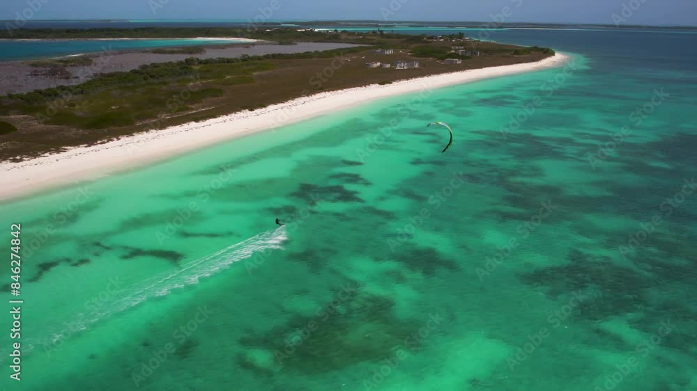 A kitesurfer navigating turquoise waters along a pristine, isolated beach, aerial view A kitesurfer navigating turquoise waters along a pristine, isolated beach, aerial view