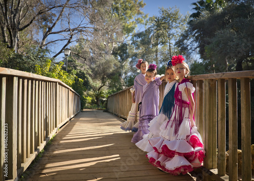 Four girls dancing flamenco, posing looking at the camera, in typical flamenco dress, on a wooden bridge. Concept dance, flamenco, typical Spanish, Seville, Spain.