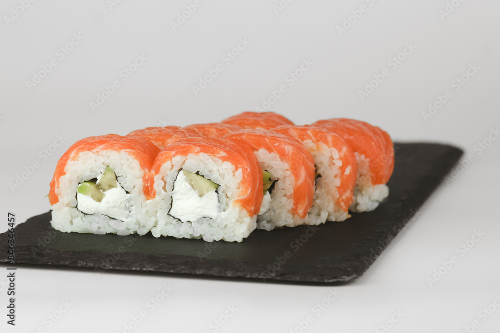 Close-up of salmon avocado sushi rolls on a black slate plate, with a white background Close-up of salmon avocado sushi rolls on a black slate plate, with a white background