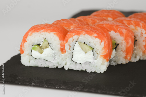 A close-up shot of a plate of freshly prepared salmon and avocado sushi rolls, arranged neatly on a black slate plate