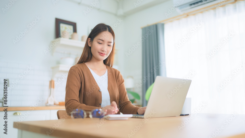 Beautiful young Asian woman working with laptop computer in home kitchen. Work at home Beautiful young Asian woman working with laptop computer in home kitchen. Work at home