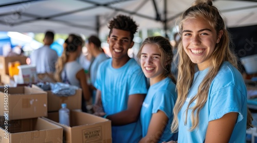 Smiling volunteers in blue shirts working at a community event, sorting donations and food items under a tent.