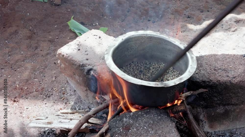 Person roasting coffee beans in an old casserole over ground fire Person roasting coffee beans in an old casserole over ground fire