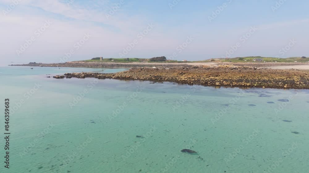 Guernsey,Channel Islands. Crystal clear waters and rocky shoreline in otherwise sandy bay with birds flying by. Low tide on sunny day. Guernsey,Channel Islands. Crystal clear waters and rocky shoreline in otherwise sandy bay with birds flying by. Low tide on sunny day.