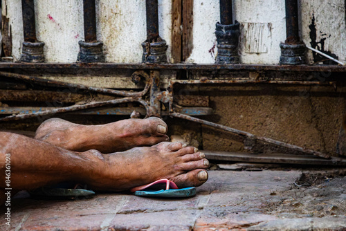 Photography The image shows bare, dirty feet resting on a dilapidated pavement outside La Bodeguita del Medio, Old Havana, highlighting the stark contrast between local hardships and the bustling tourist area