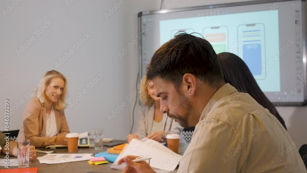 Group of business people sitting in a meeting room discussing a design for a smartphone application. Group of business people sitting in a meeting room discussing a design for a smartphone application.