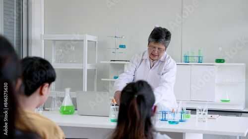 Elderly teacher stands in front classroom teaching students in science room, teacher is doing experiment as example for students see, so that students can see picture know how do experiment.
