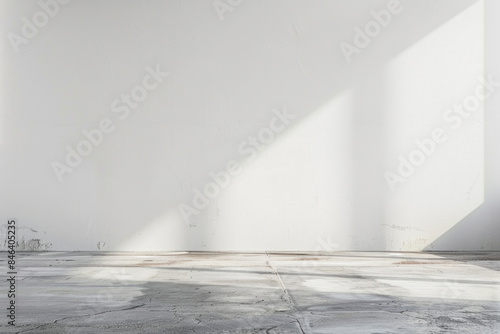 A large empty room with a white wall and a grey floor. The room is very bare and empty, with no furniture or decorations. The sunlight coming in through the window casts a shadow on the floor