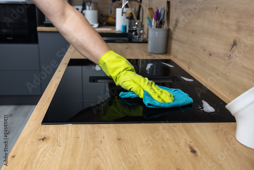 A man's hand in a protective glove washes a ceramic kitchen stove