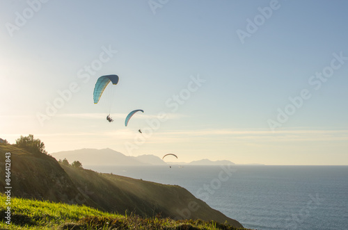 Sunset over the sea in Basque country with people doing paragliding
