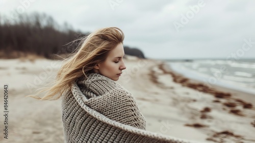 A stunning girl with long hair walks along the shore of the northern sea wrapped in a woolen blanket