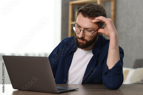 Overwhelmed man sitting with laptop at table indoors