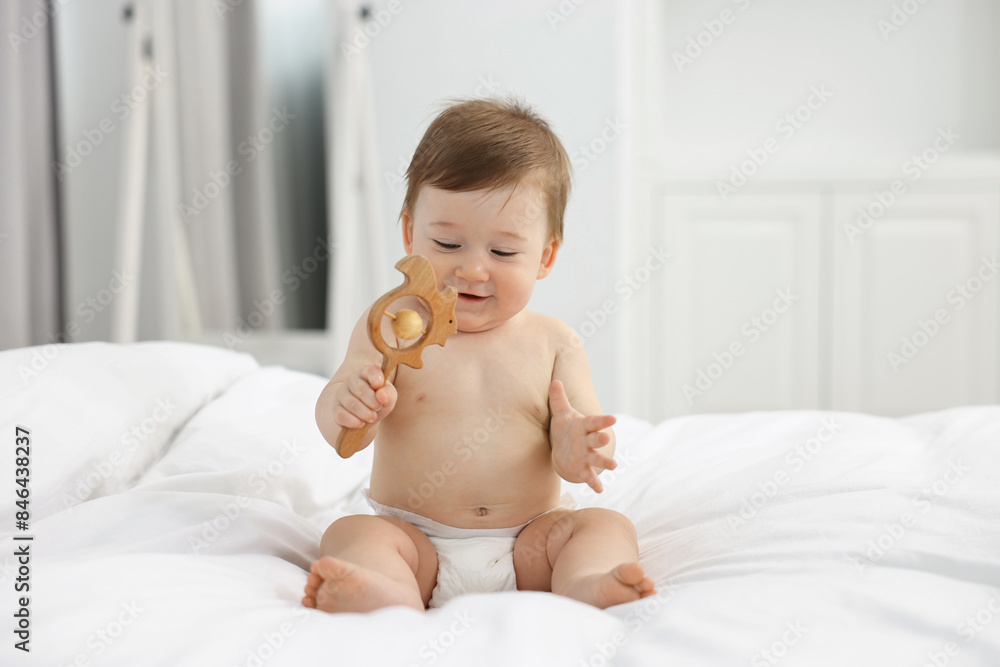 Cute baby boy with wooden rattle on bed at home Cute baby boy with wooden rattle on bed at home