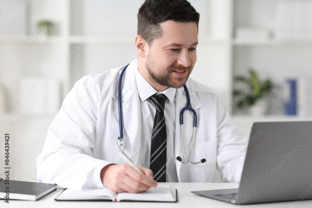 Doctor having online consultation via laptop at table in clinic Doctor having online consultation via laptop at table in clinic