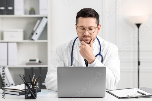 Doctor having online consultation via laptop at table in clinic