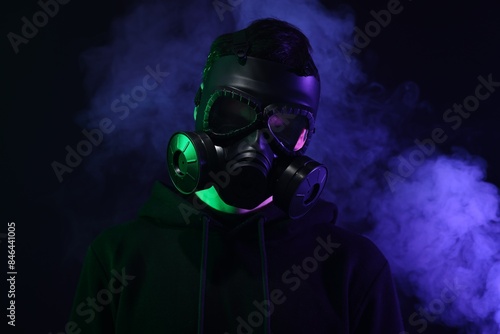 Man wearing gas mask in color lights and smoke on black background © New Africa
