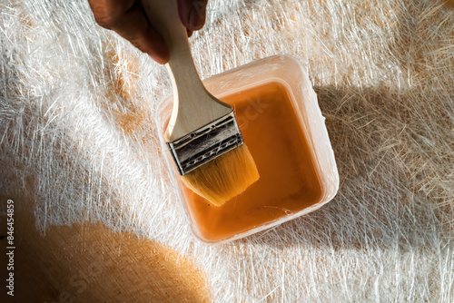 On top of the fiberglass sheet, a paintbrush inside a container containing the fiberglass solution.