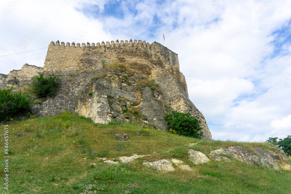 Side view of Surami fortress built on a rock. Green grass, stone walls with loopholes Side view of Surami fortress built on a rock. Green grass, stone walls with loopholes