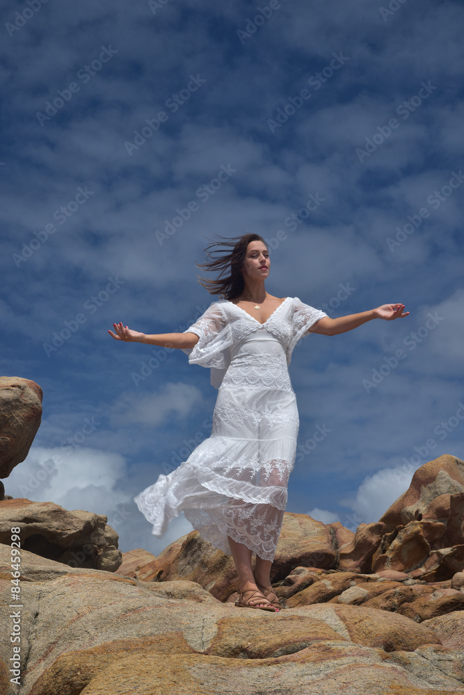 portrait of female model standing wearing white goddess dress, dramatic natural landscape background of rocky ocean shoreline with stone clifftops. castle rock, Busselton, Western Australia portrait of female model standing wearing white goddess dress, dramatic natural landscape background of rocky ocean shoreline with stone clifftops. castle rock, Busselton, Western Australia