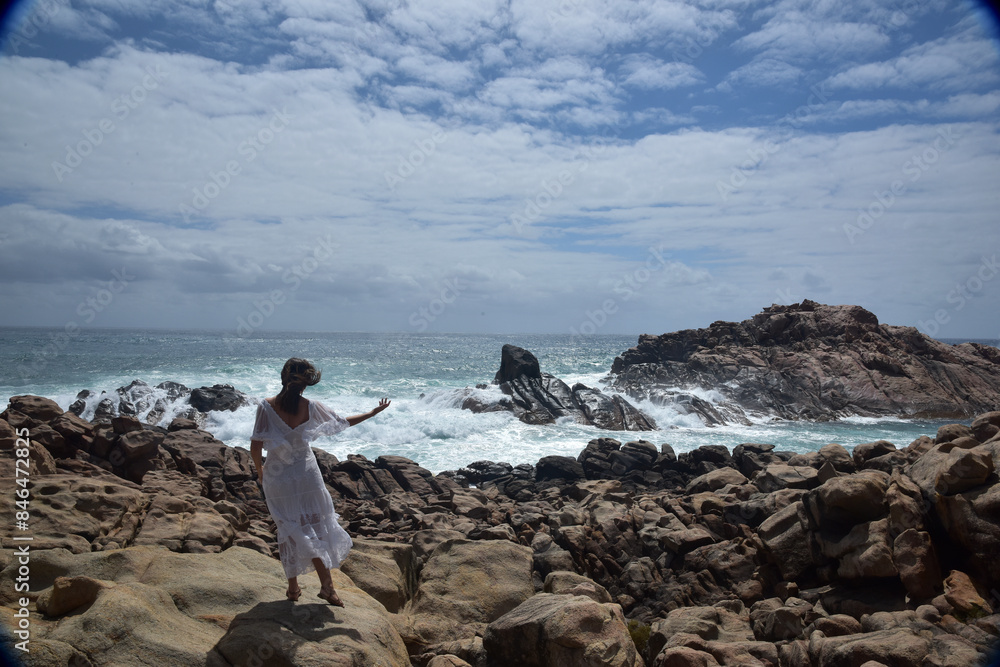 portrait of female model standing wearing white goddess dress, dramatic natural landscape background of rocky ocean shoreline with stone clifftops. castle rock, Busselton, Western Australia portrait of female model standing wearing white goddess dress, dramatic natural landscape background of rocky ocean shoreline with stone clifftops. castle rock, Busselton, Western Australia