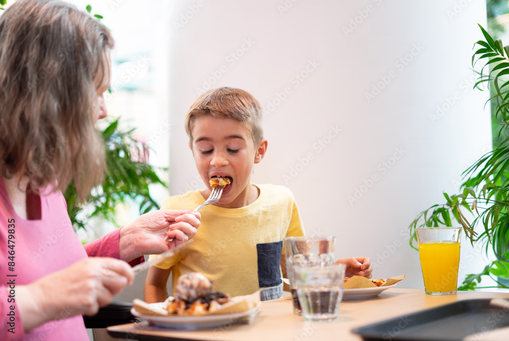 Grandmother giving her grandson a taste of her waffle in a cafe Grandmother giving her grandson a taste of her waffle in a cafe