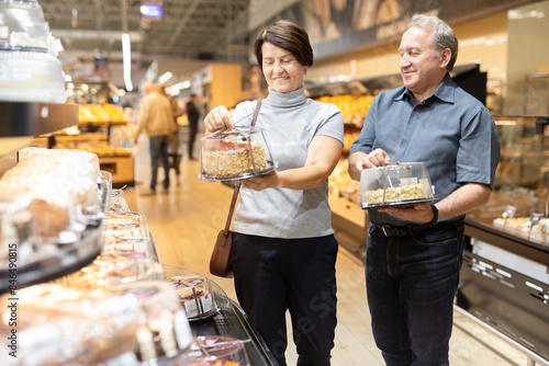 Married couple choosing fresh delicious cakes together in the grocery department of supermarket photo