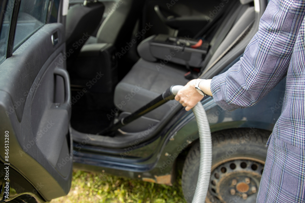 A person vacuums the backseat of a car, focusing on removing dirt and debris from the interior. The car door is open, revealing a clear view of the interior. A person vacuums the backseat of a car, focusing on removing dirt and debris from the interior. The car door is open, revealing a clear view of the interior.
