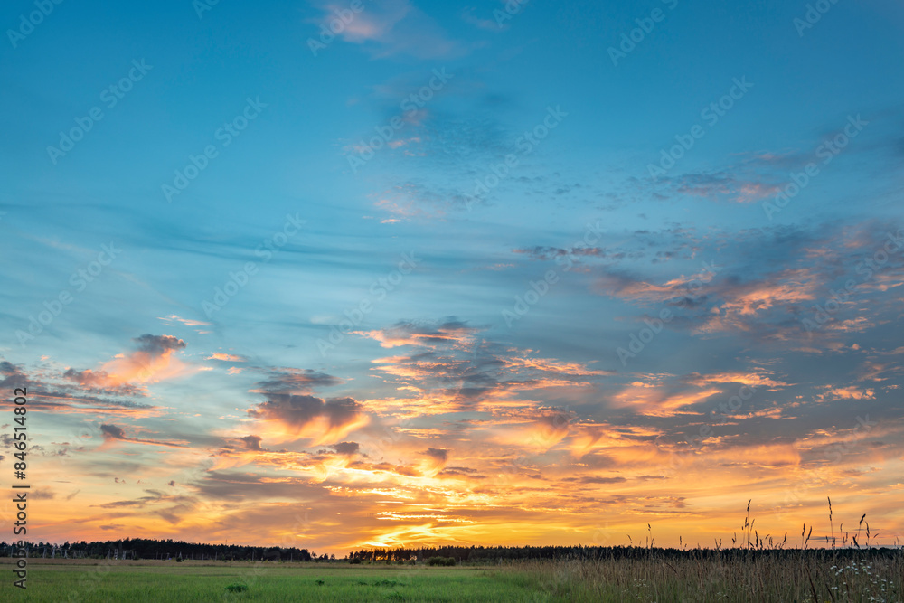 Obraz premium scenic landscape photograph captures a captivating sunset, showcasing a vibrant sky painted in hues of orange, pink, and blue, with wispy clouds streaking across the horizon.