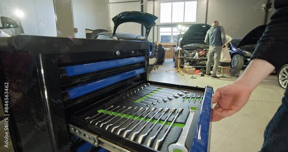 A mechanic handling tools and working on an electric car in a well-lit auto repair shop with blue tool cabinet. EV repair concept. Auto Service, Electric vehicle engine maintenance A mechanic handling tools and working on an electric car in a well-lit auto repair shop with blue tool cabinet. EV repair concept. Auto Service, Electric vehicle engine maintenance