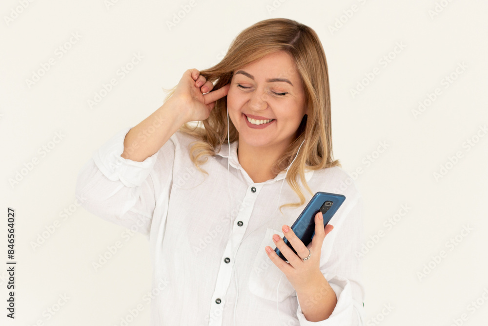 Image of a happy young beautiful woman posing isolated over white wall background listening music with earphones using mobile phone. Image of a happy young beautiful woman posing isolated over white wall background listening music with earphones using mobile phone.